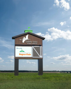 A large sign reading Sandhills Global Event Center stands in an open field with a bright blue sky.